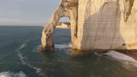 Flying-trough-a-natural-rock-arch-of-Etretat.-Normandy-France,-drone-view-sunset